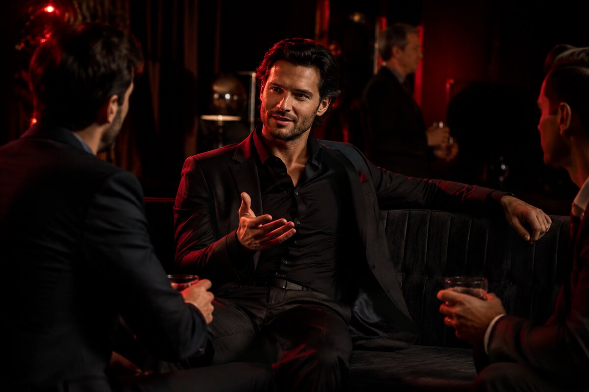 a well-dressed man using relaxed open posture and controlled gestures in a sophisticated gathering